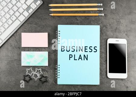 Notebook with text BUSINESS PLAN, office stationery and smartphone on gray background Stock Photo