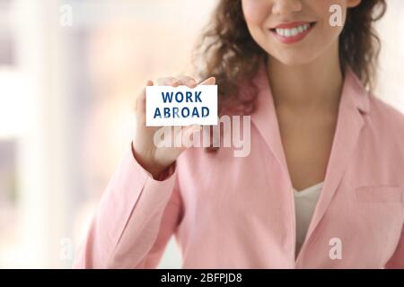 Young woman holding business card with text WORK ABROAD on blurred background. Recruitment concept Stock Photo