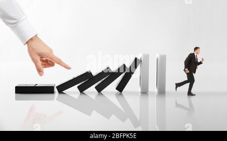 Man running from falling huge dominoes while male hand pushing them on light background. Concept of irresponsible business strategy Stock Photo