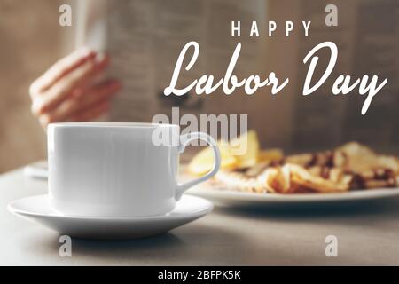 Cup of coffee and breakfast on table. Text HAPPY LABOR DAY on blurred background Stock Photo