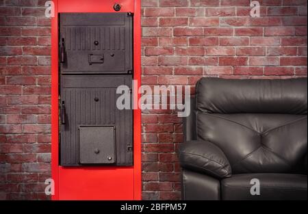 Energy savings concept. Solid fuel boiler and armchair against brick wall background Stock Photo