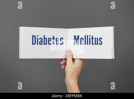 Health care concept. Woman holding brochure with text DIABETES MELLITUS on gray background Stock Photo