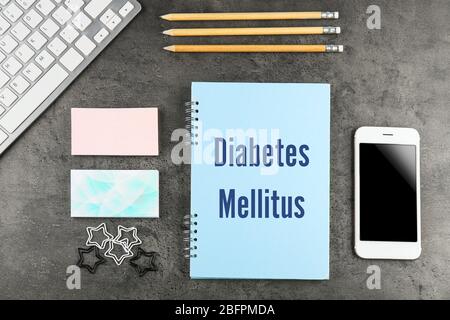 Health care concept. Notebook with title DIABETES MELLITUS, phone and stationery on gray background Stock Photo