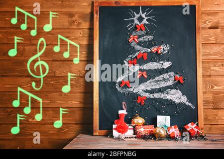 Chalkboard with drawn fir tree, garland and notes on wooden background. Concept of Christmas music and songs Stock Photo