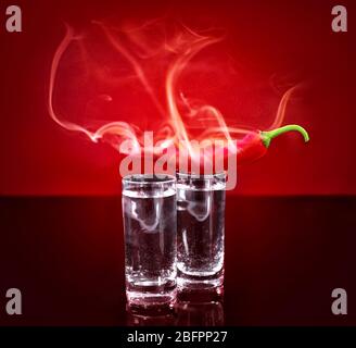 Smoking chili pepper and glasses with vodka on red background Stock Photo