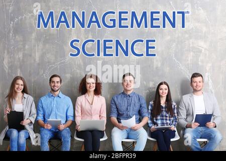 Concept of management science. Young people sitting on chairs against grunge wall background Stock Photo