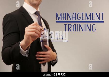 Concept of management training. Young man drawing diagram on virtual screen against color background Stock Photo