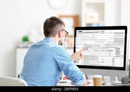 Man using computer for filling in individual income tax return form at table Stock Photo