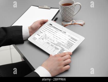 Man using tablet for filling in individual income tax return form at table Stock Photo