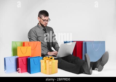 Internet shopping concept. Man with laptop and purchases on light background Stock Photo
