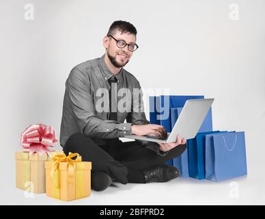 Internet shopping concept. Man with laptop and purchases on light background Stock Photo