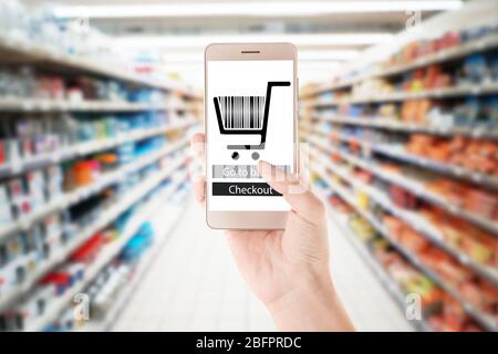 Woman holding smartphone and blurred shelves with different products on background. Internet shopping concept Stock Photo