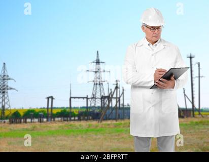 Senior engineer with clipboard and electric substation on background Stock Photo
