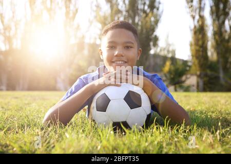 African-American boy with soccer ball lying on green grass in park. Football concept Stock Photo