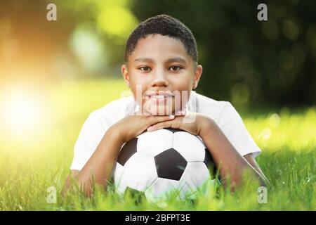 African-American boy with soccer ball lying on green grass in park. Football concept Stock Photo