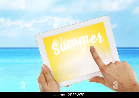 Man using tablet and ocean on background. Word SUMMER on screen Stock Photo