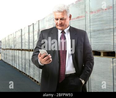 Mature manager using smartphone near goods, outdoors. Wholesale and logistic concept Stock Photo