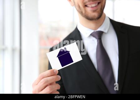 Real estate agent holding business card with drawing of house on blurred background Stock Photo