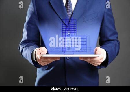 Real estate agent holding tablet and projection of building on dark background Stock Photo