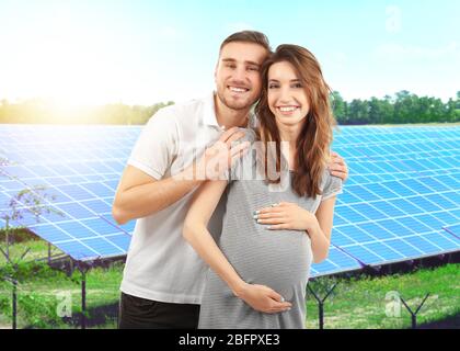 Young man with pregnant wife and solar panels on background Stock Photo
