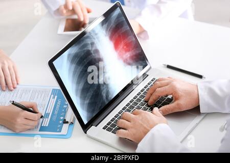 Doctor working with laptop at table in hospital. X-ray image of chest on screen. Lung cancer concept Stock Photo