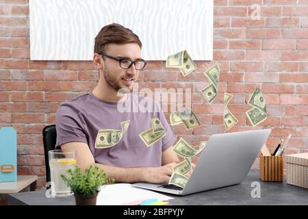 Money flying out of laptop while man using it at table in office Stock Photo