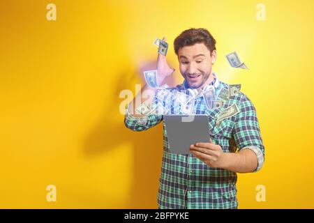 Money flying out of tablet while man using it on yellow background Stock Photo