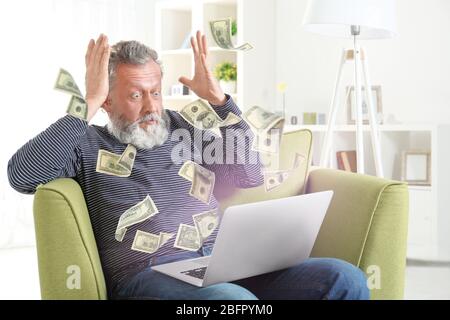 Money flying out of laptop while senior man using it at home Stock Photo