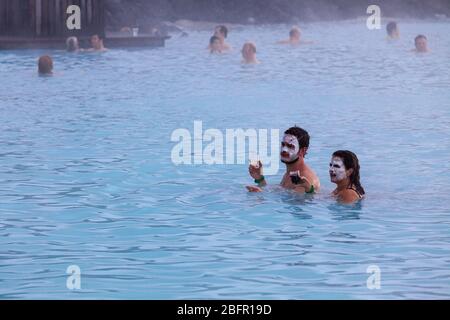 A couple drink beer in the Blue Lagoon Geothermal Spa Pool near Reykjavik in Iceland with steam rising off it on a cold day in winter Stock Photo