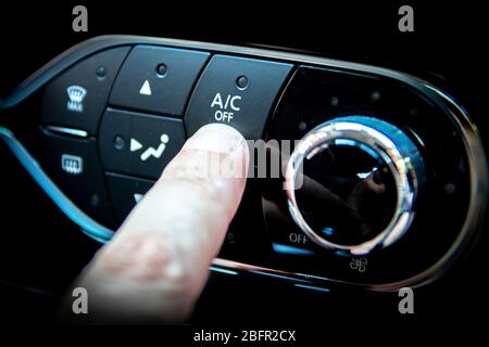 A finger pressing the A/C or air conditioning button on the dashboard of a car Stock Photo