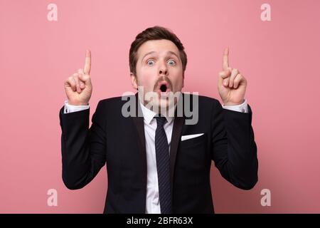 Young and handsome businessman pointing up with his fingers. Studio shot on pink wall. Stock Photo