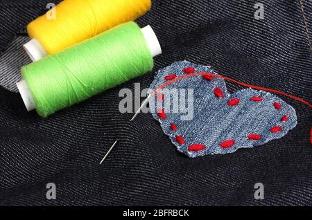 Heart-shaped patch on jeans with threads and needle closeup Stock Photo