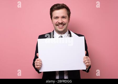 Attractive mature man with funny mustache in business suit with blank sign. Studio shot on pink wall. Stock Photo