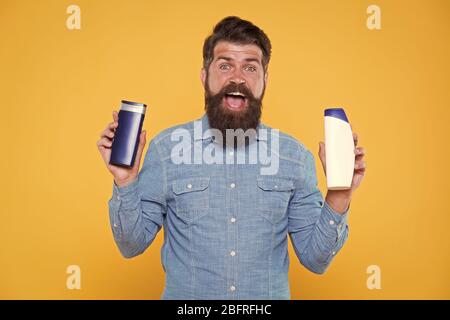 Grooming at every opportunity. Bearded man hold shampoo bottles yellow background. Cosmetics and toiletries. Hygiene and personal grooming. Male body grooming and skincare. Grooming products for men. Stock Photo