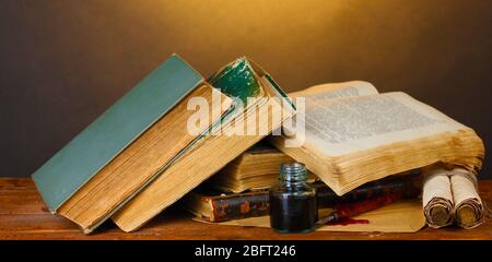 old books, scrolls, ink pen and inkwell on wooden table on brown background Stock Photo