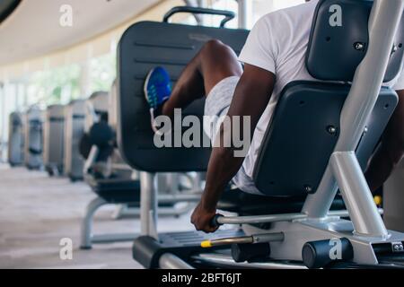 Back view of African American man doing exercise on leg press during fitness training in modern gym. Stock Photo