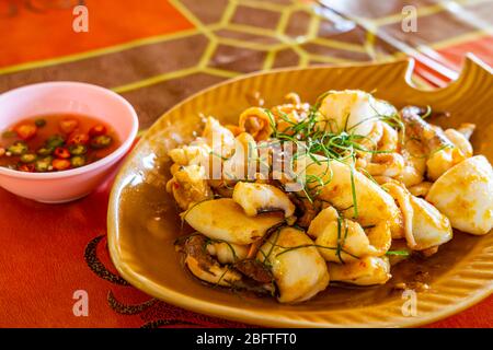 Stir-fried squid with boiled salted duck egg yolk in a brown dish on a table. Stock Photo
