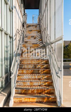 Outside metal, rusty steps with shadows from the sunshine upon them and blue sky at the top of them Stock Photo