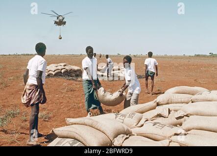 1993 - Men from the village of Maleel stack bags of wheat as a Marine Heavy Helicopter Squadron 363 (HMH-363) CH-53D Sea Stallion helicopter prepaers to drop another load during the multinational relief effort OPERATION RESTORE HOPE.
