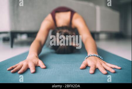 Yoga home stretching meditation woman doing childs pose warm up stretch in living room home. Hands touching floor exercise mat and mala bracelet. Fitness relaxation stress- free concept. Stock Photo