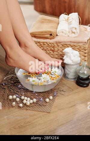 Pedicured feet of young woman over bowl with hot water, aroma oil and flowers in spa salon Stock Photo