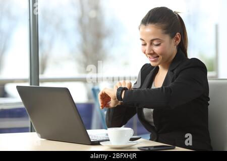 Happy entrepreneur woman checking smartwatch sitting in a coffee shop Stock Photo