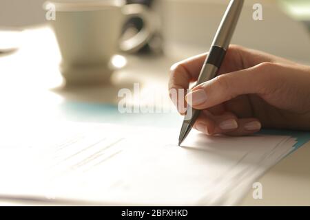 Close up of woman hands signing contract sitting on a desk at night Stock Photo