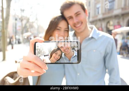 Happy couple taking selfie showing blank smart phone screen posing in the street Stock Photo