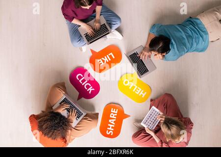 Above view of young people sitting and lying on floor with internet activity tags and using modern portable devices, social media addiction concept Stock Photo