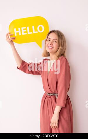 Portrait of positive attractive young woman in pink jumpsuit showing communication tag while saying Hello Stock Photo