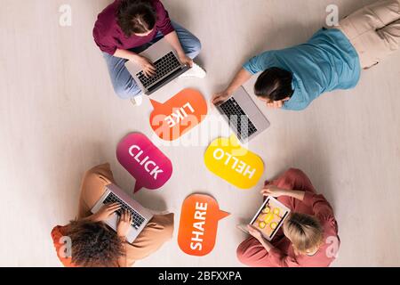 Above view of internet users using modern devices while interacting online, colorful Like, Hello, Share, Click tags on floor Stock Photo