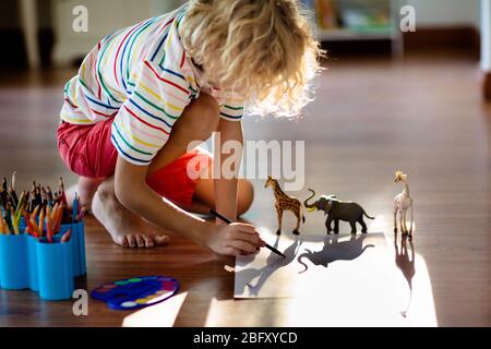 Child shadow drawing animals. Kids play at home. Fun crafts for kindergarten children. Little boy painting giraffe and elephant in sunny bedroom. Game