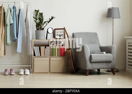 Full length view at studio apartment interior with minimal design, focus on comfy grey armchair and clothes rack against white wall, copy space Stock Photo