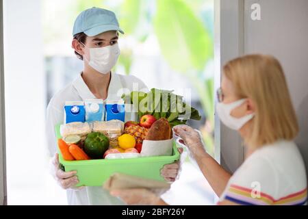 Food delivery during corona virus outbreak. Courier wearing face mask delivering grocery order in coronavirus epidemic. Safe shopping in pandemic. Tak Stock Photo